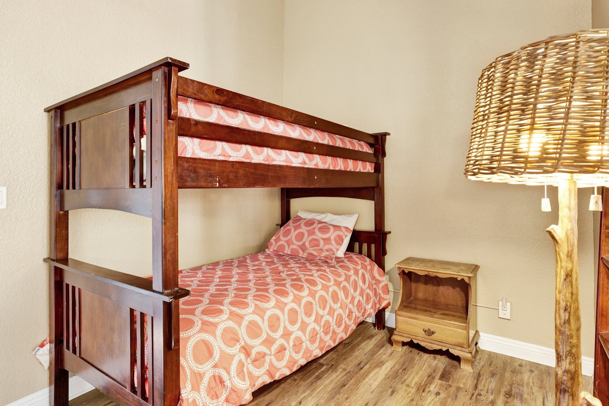 A single wooden bunk bed with a patterned bedspread, a small wooden nightstand, and a woven lamp.