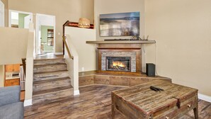 Ein Wohnzimmer mit Kamin, Holzboden, einer Treppe und einem flachbildfernseher, der über dem Kamin angebracht ist.