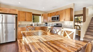 Eine Küche mit Holzschränken, einem Edelstahl-Kühlschrank, einer Mikrowelle und einem großen Esstisch aus Holz.