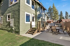 Ein zweistöckiges Haus mit einer Terrasse und Gartenmöbeln.