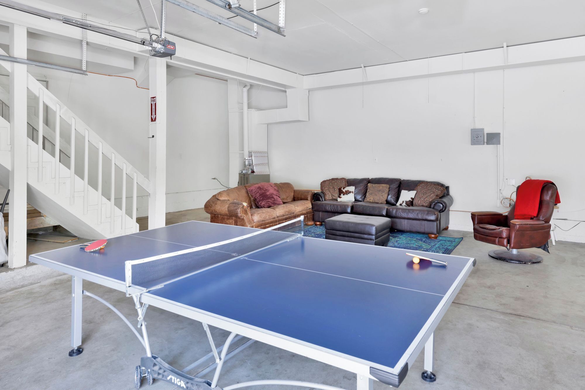 A spacious room with a ping pong table, a brown leather sofa, and a red armchair.