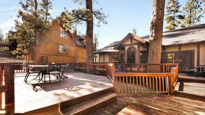A wooden deck with outdoor furniture, surrounded by trees and buildings. - Four Happy Bears Estate #1277 (Big Bear Lake)