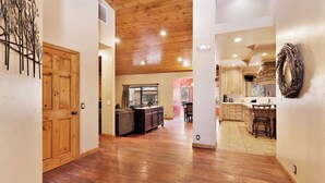 A spacious hallway with wooden flooring leading to a kitchen area with wooden cabinets and a dining area. - Four Happy Bears Estate #1277 (Big Bear Lake)