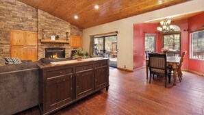 A spacious living area with a stone fireplace, wooden ceiling, and a dining area with a red accent wall. - Four Happy Bears Estate #1277 (Big Bear Lake)