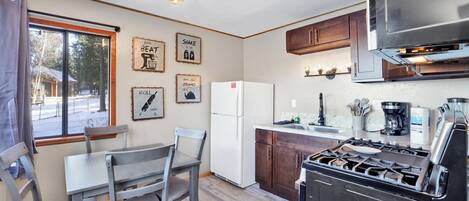 A compact kitchen with a gas stove, white refrigerator, and wooden cabinets. There are framed motivational posters on the wall and a window with a view of a snowy landscape.