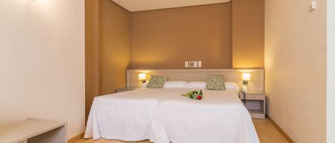 A hotel room with two beds, a bedside table, a nightstand, and a wall-mounted phone.