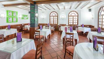 Un ristorante con travi in legno, pareti bianche e ampie finestre ad arco. I tavoli sono apparecchiati con tovaglie bianche e sedie.
