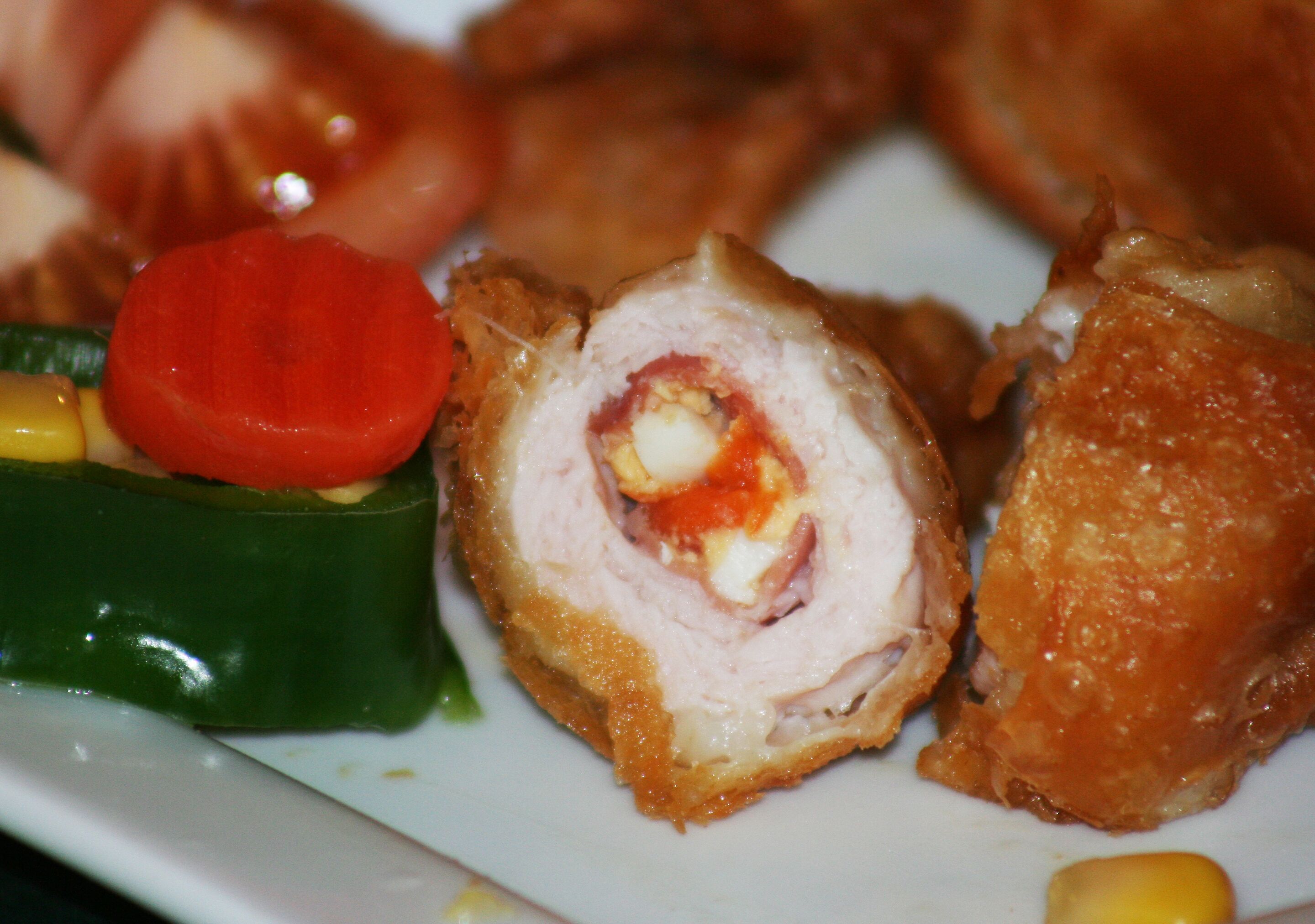 A plate with a stuffed meat dish, a slice of tomato, and a piece of green vegetable.