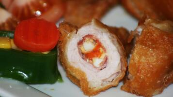 A plate with a stuffed meat dish, a slice of tomato, and a piece of green vegetable.
