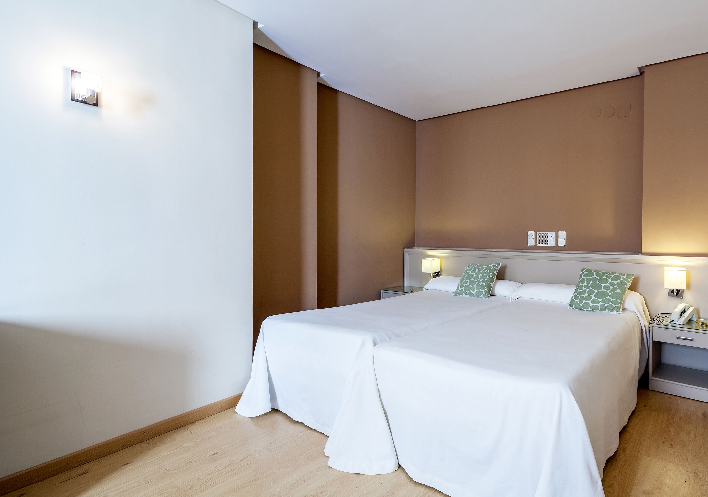 A double bed with white bedding, two bedside tables with lamps, and a headboard with a light fixture.