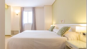 Ein Hotelzimmer mit zwei Betten, einem Nachttisch, einer Lampe und einem Vorhangfenster.