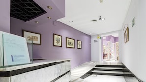 Eine Hotellobby mit einer Rezeption, gerahmten Kunstwerken an den Wänden und einer Treppe zu einem weiteren Bereich.