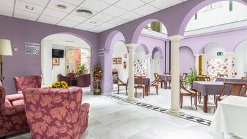 Un vestíbulo de hotel con paredes moradas, piso de baldosas y una zona de estar con sofás de estampado floral.