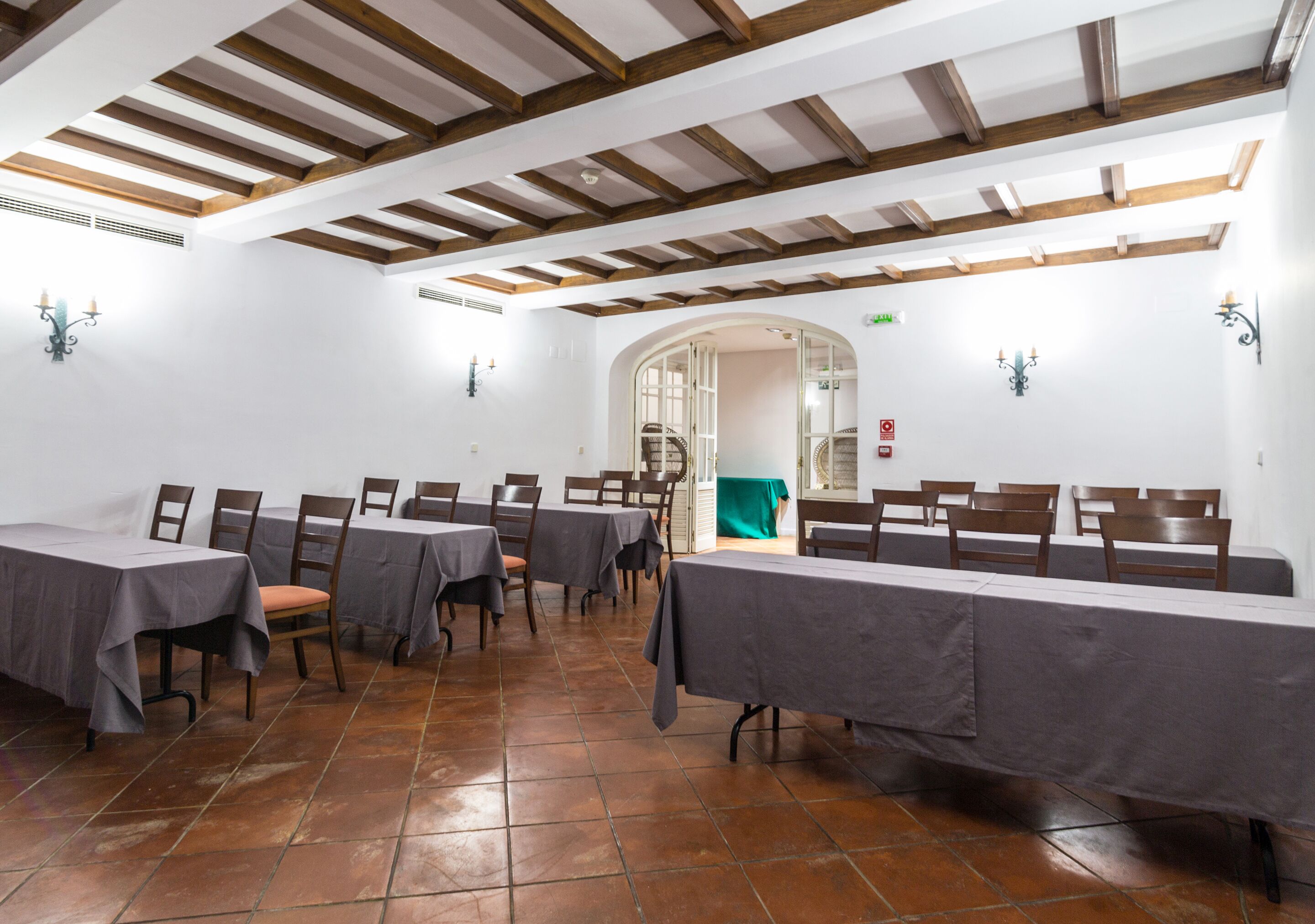 Un comedor con mesas y sillas, suelo de baldosas y vigas de madera en el techo.