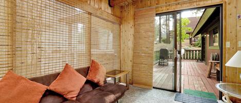 Un interior de madera con un sofá marrón, una mesita y una puerta de vidrio que da al exterior.