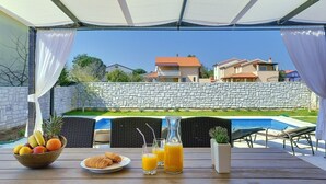 An outdoor dining area with a table set for breakfast, a pool, and a stone wall in the background. - Villa with private pool, 4 bikes just 590 meters to the pebble beach (Valbandon)