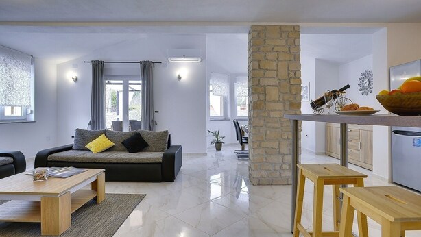 A modern living room with a sofa, coffee table, and a kitchen area with a stone column and bar stools. - Villa with private pool, 4 bikes just 590 meters to the pebble beach (Valbandon)