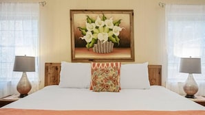 A hotel room with a large bed, two bedside lamps, a framed floral artwork above the bed, and sheer curtains on the windows. - Azure 2- Lakefront w/ Shared Pool & Dog Friendly (Kingsland)