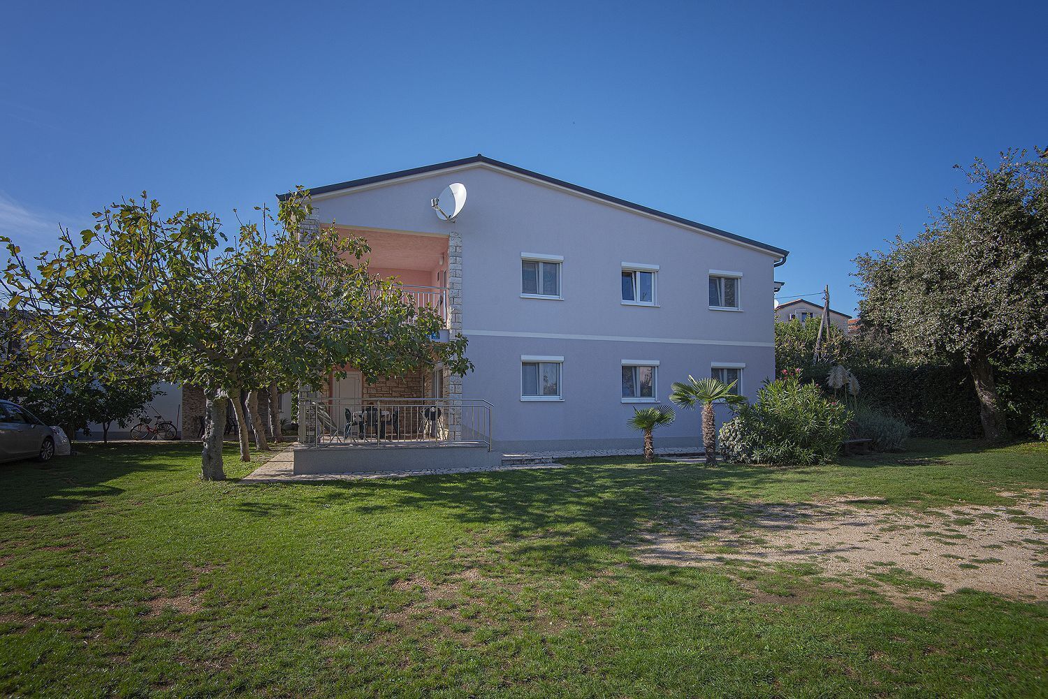 A two-story building with a balcony, a satellite dish, and a well-maintained lawn.