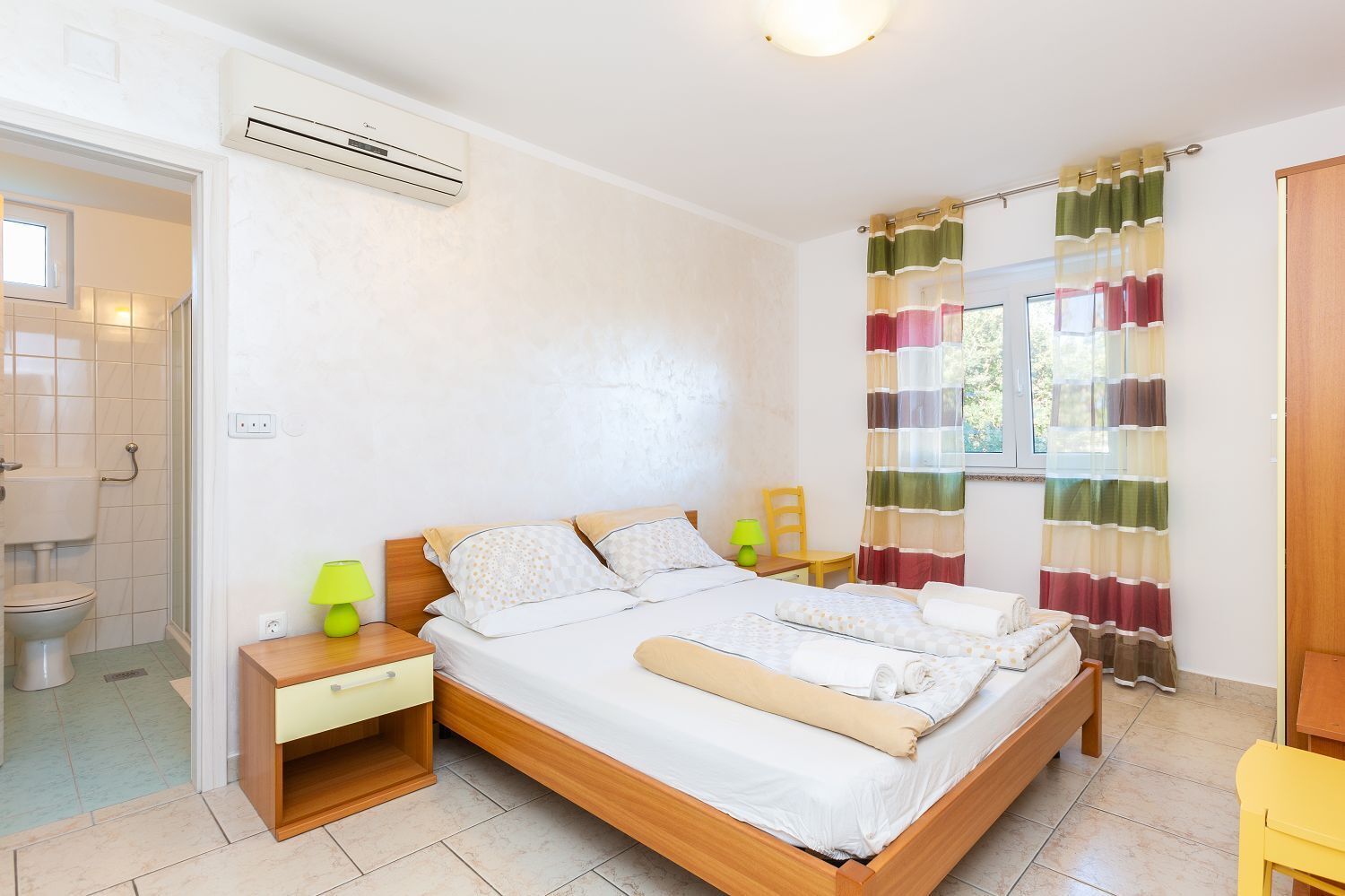 A bedroom with a wooden bed, a bedside table, a lamp, and a window with curtains.