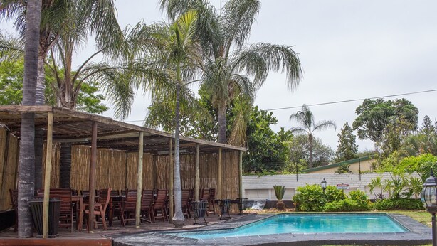 A pool area with a covered seating area and palm trees. - Big Ben Lodge (Polokwane)