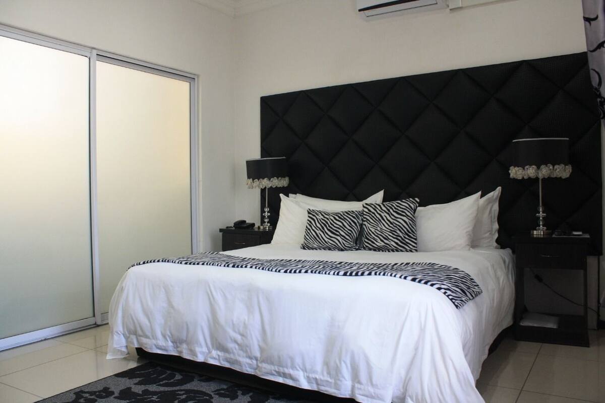 A bedroom with a large bed, black headboard, white bedding, two bedside tables with lamps, and a sliding door to the left.