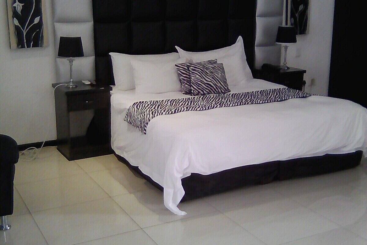 A bedroom with a large bed, a headboard with a tufted design, two bedside tables with lamps, and artwork on the walls.