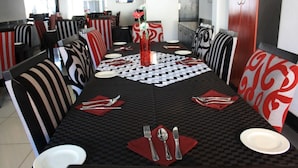 A dining area with a checkered tablecloth, striped chairs, and a vase with flowers. - Big Ben Lodge (Polokwane)