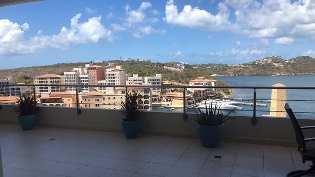 A balcony with potted plants, a view of a coastal town, and a clear sky. - Blue Residences at Blue Mall (Lowlands)