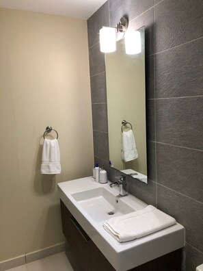 Un baño con lavamanos doble, un espejo grande y dos toallas colgadas en ganchos.