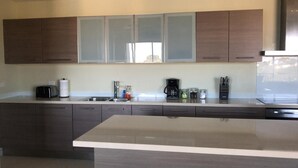 A modern kitchen with dark cabinets, a large island, a coffee maker, and a knife block. - Blue Residences at Blue Mall (Lowlands)