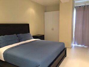 Un dormitorio con cama, mesita de noche, armario y ventana con cortinas.