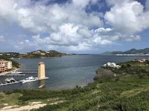 Vista costera con una torre, puerto deportivo y edificios a lo largo de la orilla.