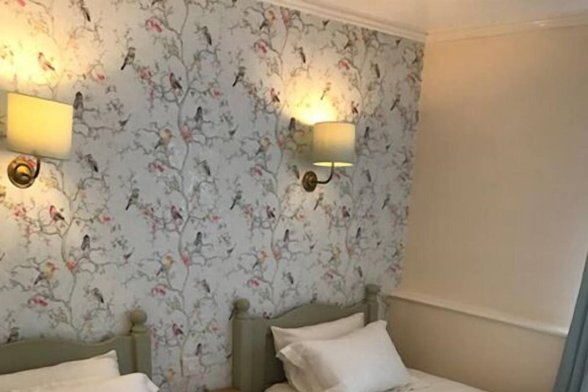 Ein Hotelzimmer mit zwei Einzelbetten, einem Nachttisch und blumigem Wandpapier.