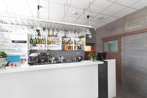 Un espace bar équipé d’une machine à café, d’étagères remplies de bouteilles et de verres suspendus.
