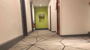 A hallway with a geometric patterned carpet, a green wall at the end, and a fire extinguisher mounted on the wall. - Enzo Hotels Contrexéville (Contrexéville)