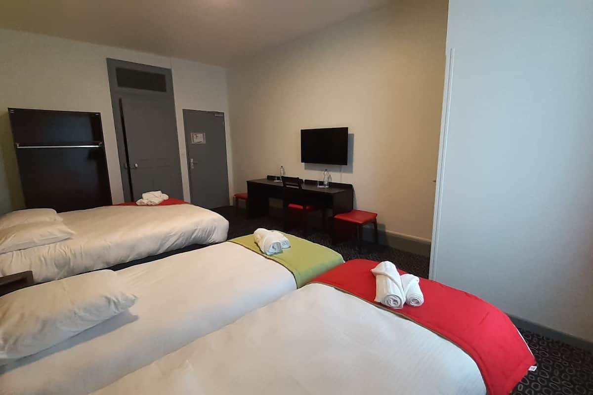 A hotel room with two beds, a desk, a television, and two doors.