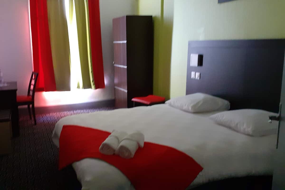 A hotel room with a large bed, a desk, a chair, and a wardrobe.
