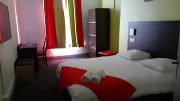 A hotel room with a large bed, a desk, a chair, and a wardrobe.