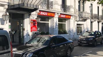Un bâtiment portant l’enseigne « ENZO HOTEL », des voitures garées et un lampadaire.