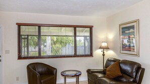 A living room with two leather sofas, a small round table, a lamp, and a window with blinds. - Shell Studios Hallandale Beach (Hallandale Beach)