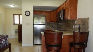 A compact kitchen with wooden cabinets, a stainless steel refrigerator, a microwave, and two bar stools. - Shell Studios Hallandale Beach (Hallandale Beach)