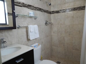 A bathroom with a sink, toilet, and shower. There is a towel rack with two towels and a toilet paper roll on a shelf. - Shell Studios Hallandale Beach (Hallandale Beach)