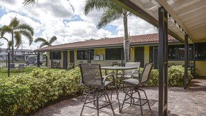 An outdoor patio area with a brick floor, metal-framed chairs, and a table. - Shell Studios Hallandale Beach (Hallandale Beach)