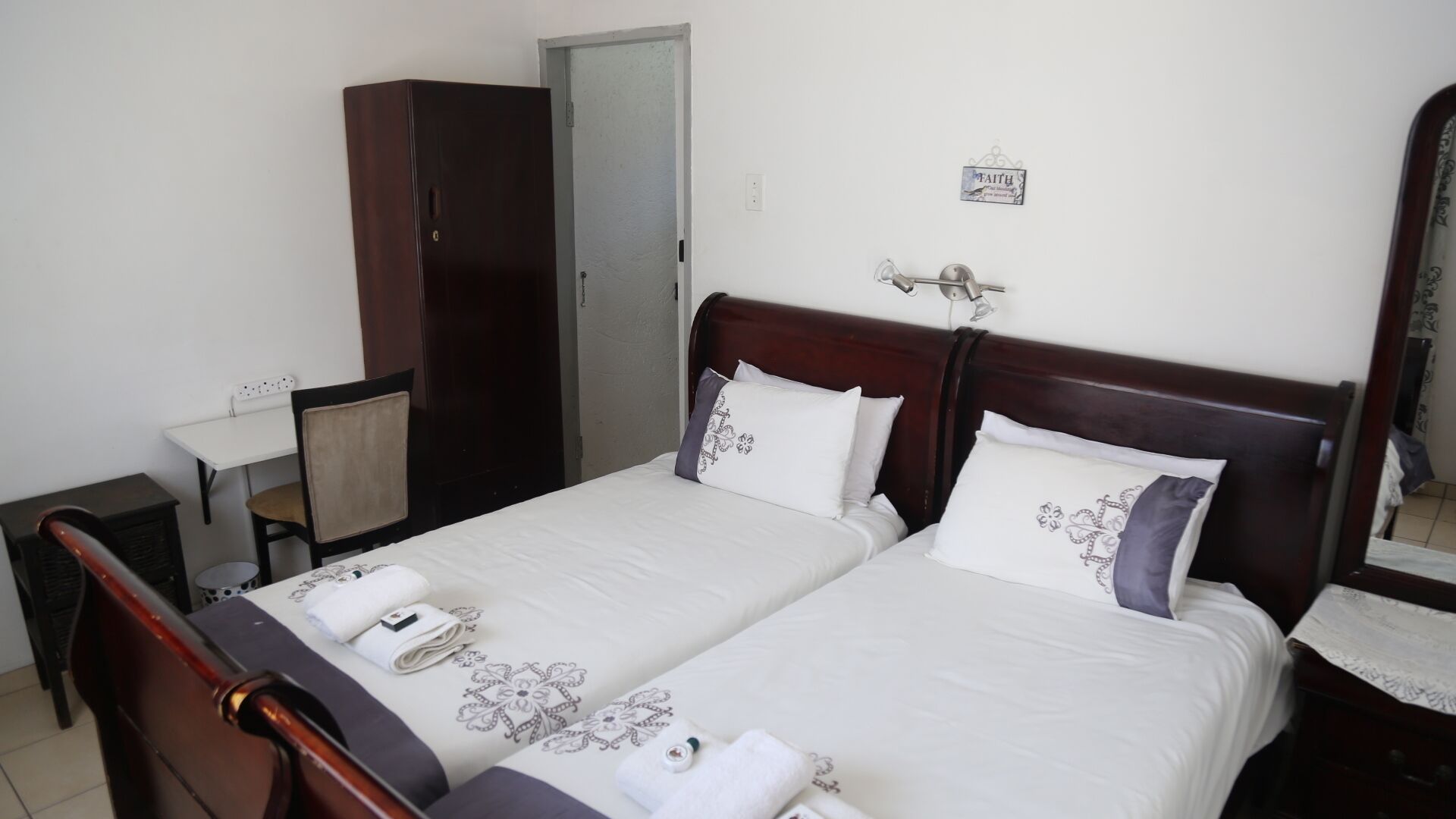 A hotel room with two beds, a wardrobe, a desk, and a mirror.