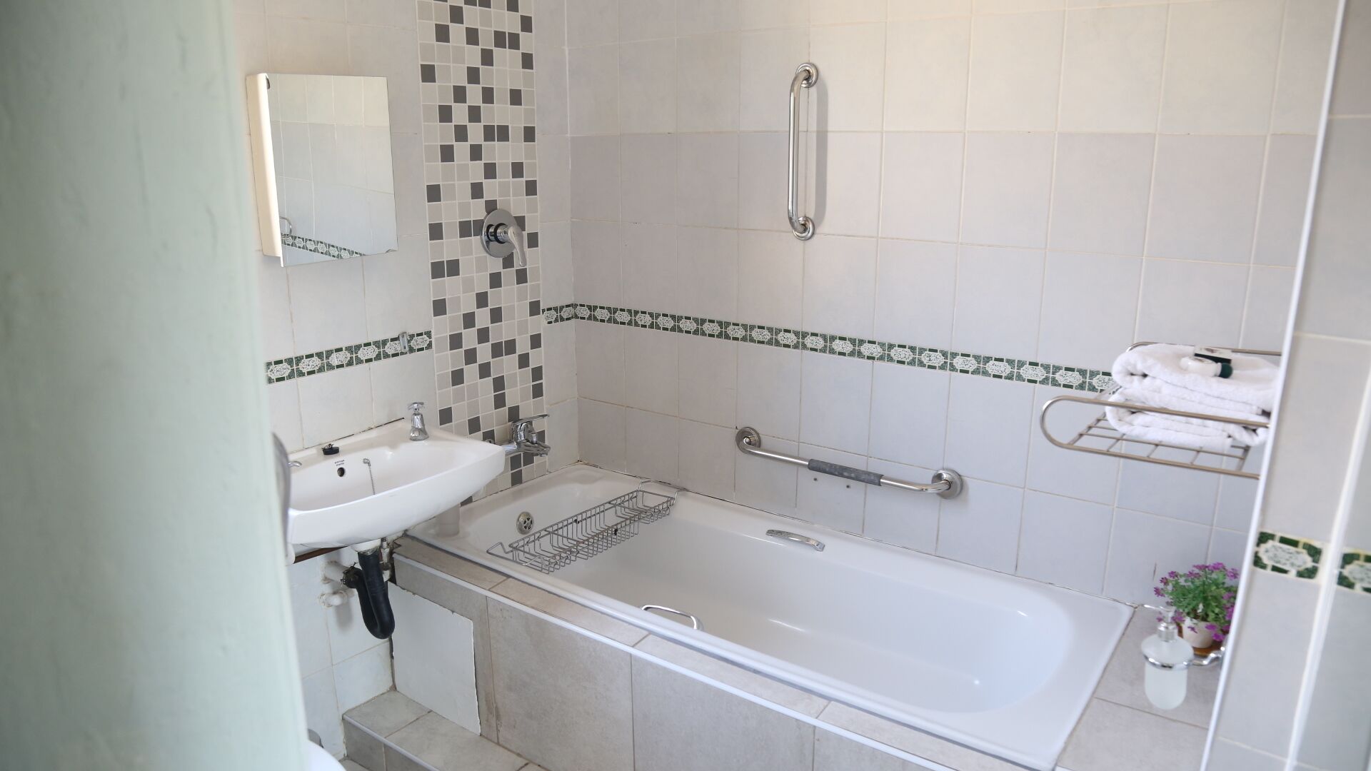A bathroom with a bathtub, a sink, and a shower. There are grab bars installed for safety.