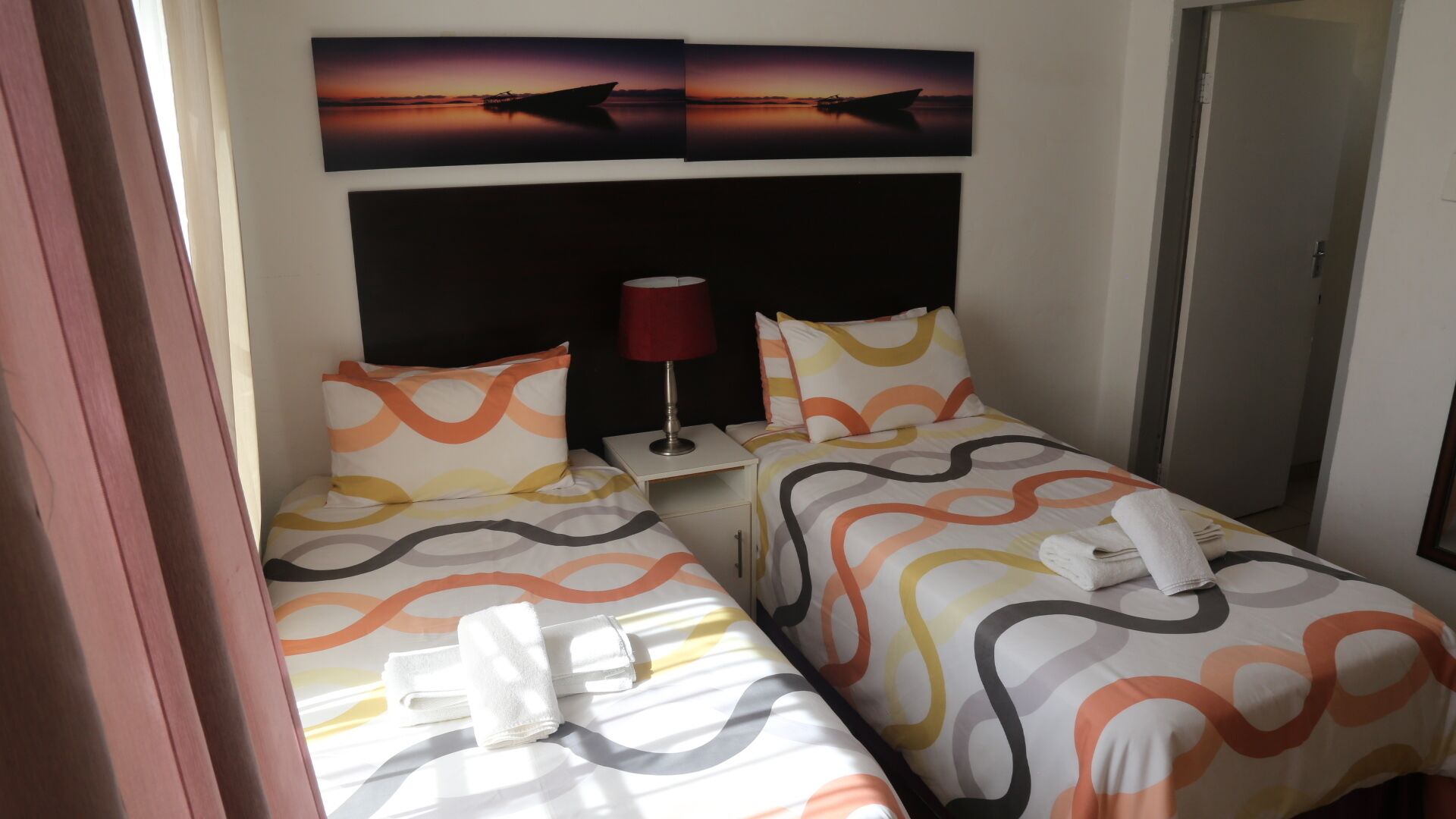 Une chambre d’hôtel avec deux lits, chacun recouvert d’une couvre-lit à motifs, une table de chevet avec une lampe et une œuvre d’art fixée au mur représentant un bateau sur l’eau.