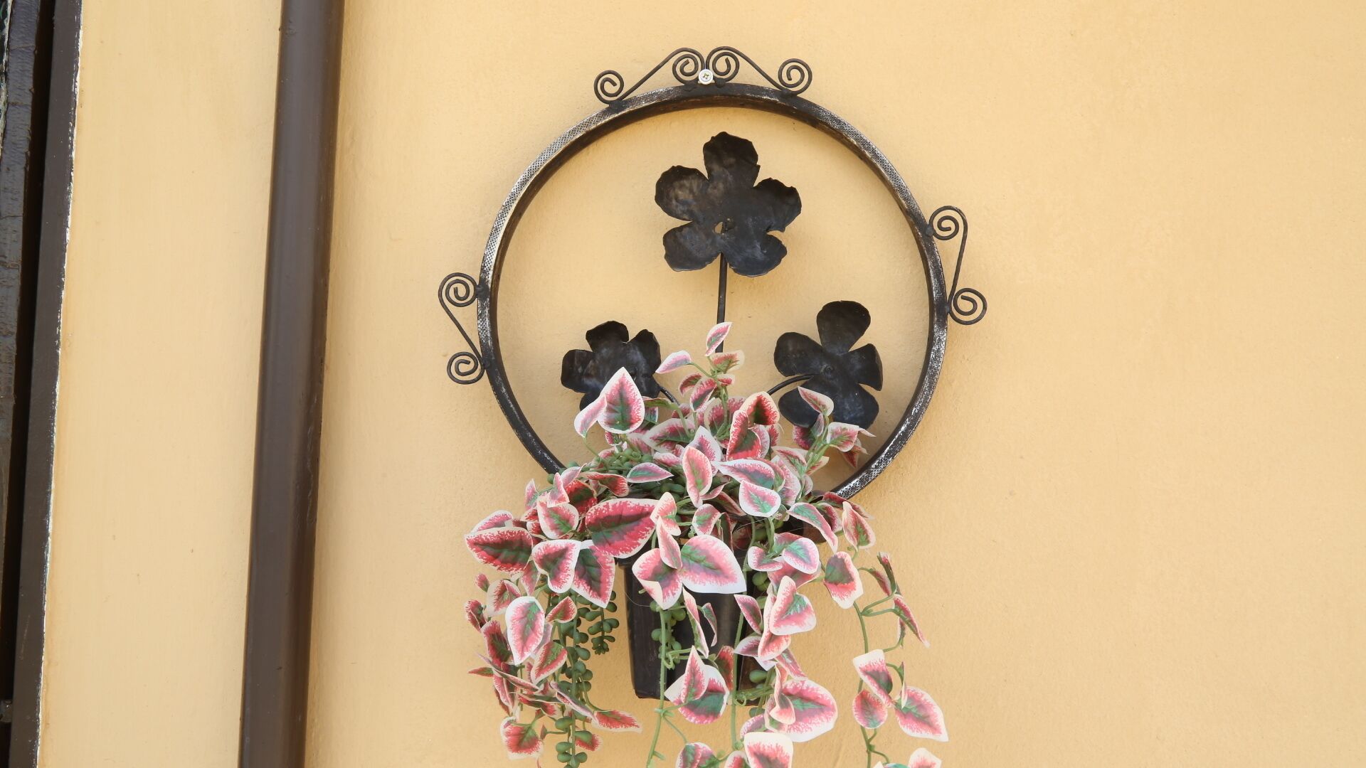 Uma obra de arte de metal fixada na parede, com moldura circular, apresentando três desenhos de flores e folhagem rosa e branca pendurada.
