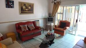 A living room with a red sofa, a glass coffee table, and a television. - Roba Monakedi Guest Lodge (Mahikeng)