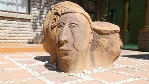 Una escultura de piedra en un entorno exterior, con un muro de ladrillo y suelo de baldosas.